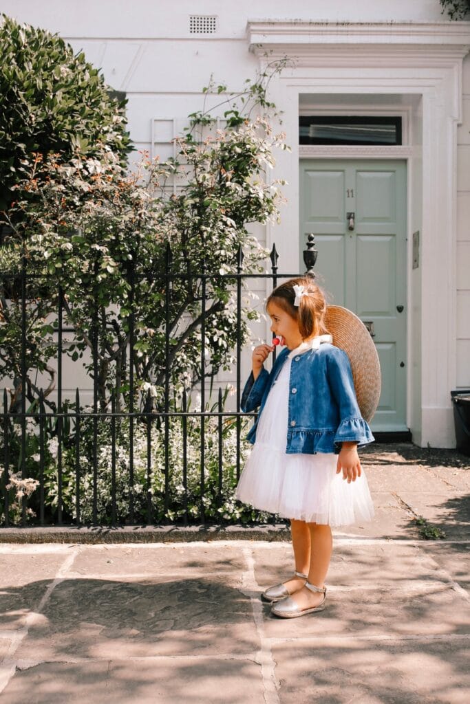 Little girl dressed elegantly in a dress with a lollipop in a stylish city