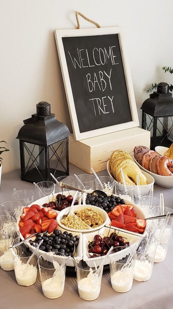 A fruit and yogurt parfait station with strawberries, blueberries, cherries, granola, and yogurt at a baby shower.