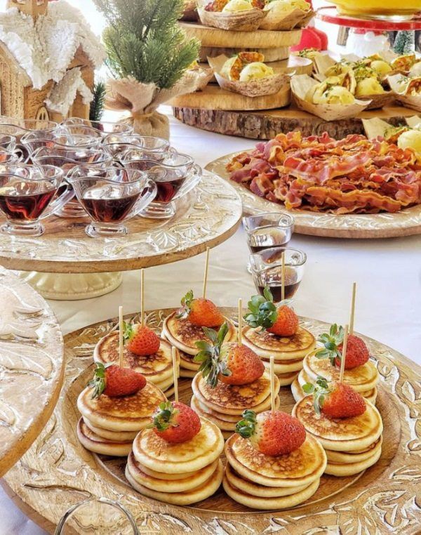 Mini pancakes with strawberries served at a baby shower brunch with cups of syrup on the side.