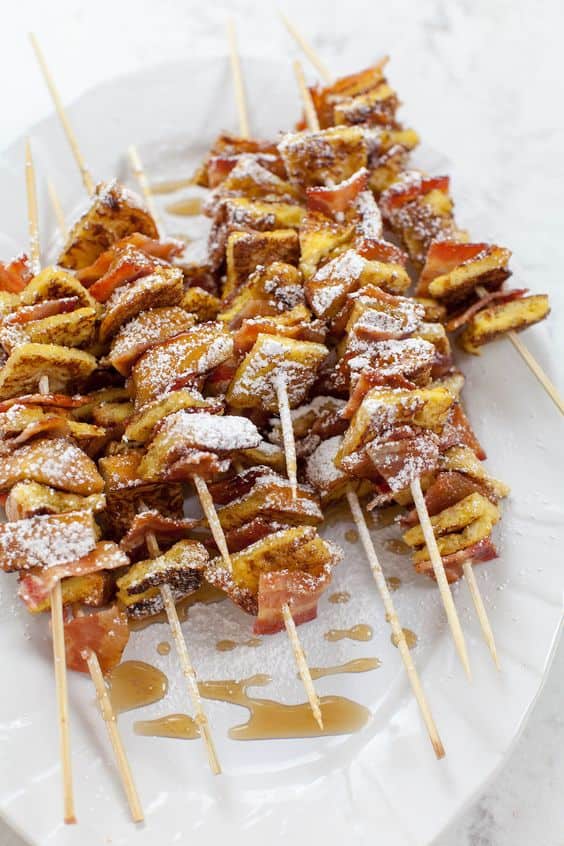 French toast and bacon skewers topped with powdered sugar and served with syrup for a baby shower brunch.