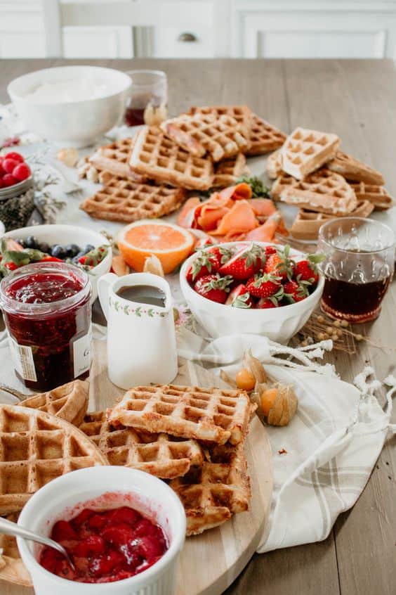A waffle bar for a baby shower featuring waffles, fresh fruit, syrup, and jam toppings.